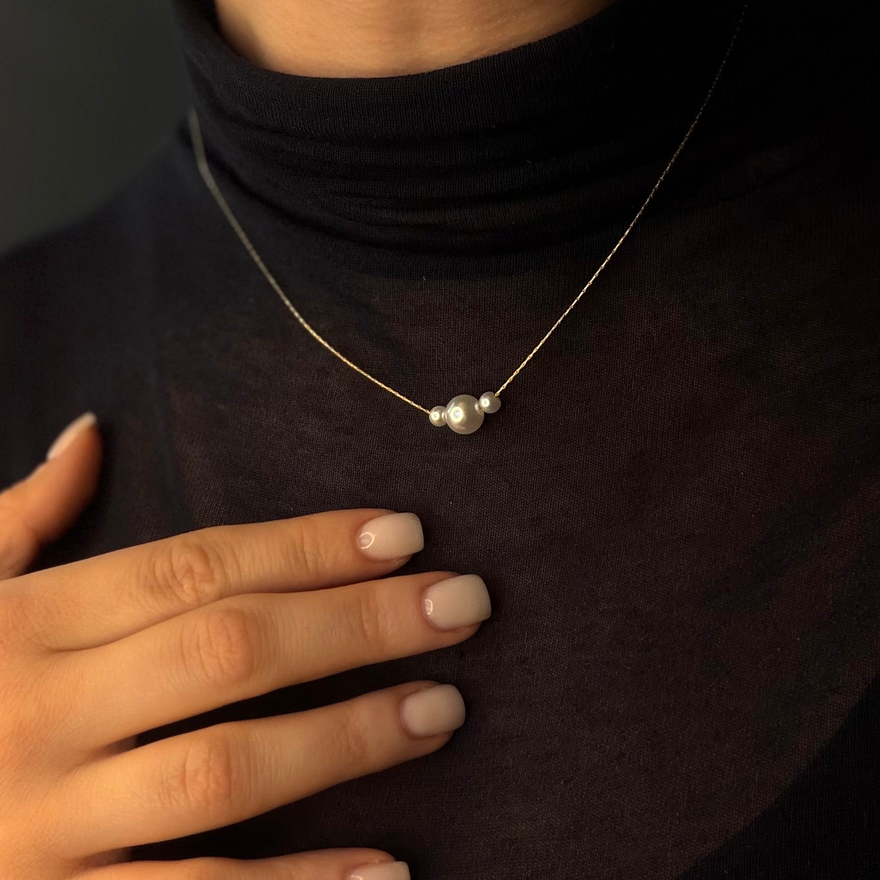 Person wearing a delicate necklace with a small pendant, hand resting on chest.