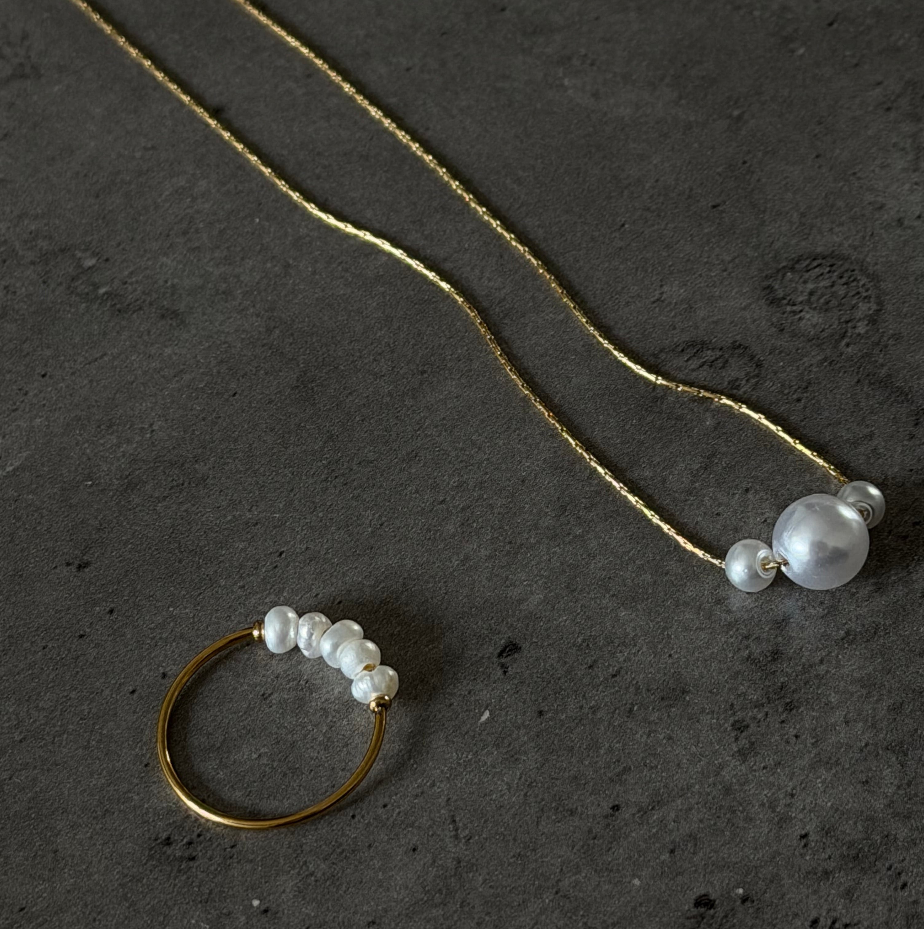 Gold necklace and ring with pearls on a dark textured surface