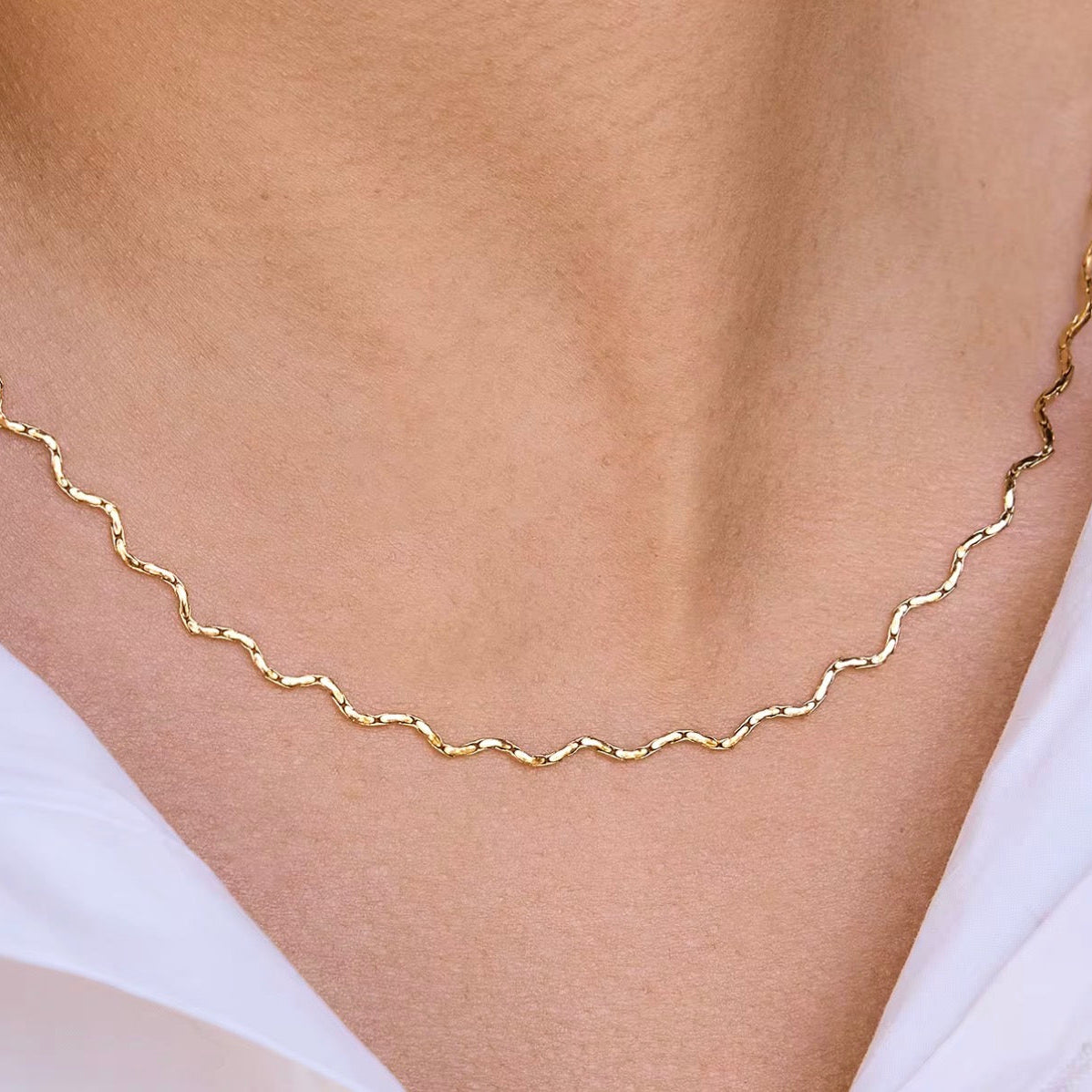 Gold necklace on a person wearing a white top against a neutral background