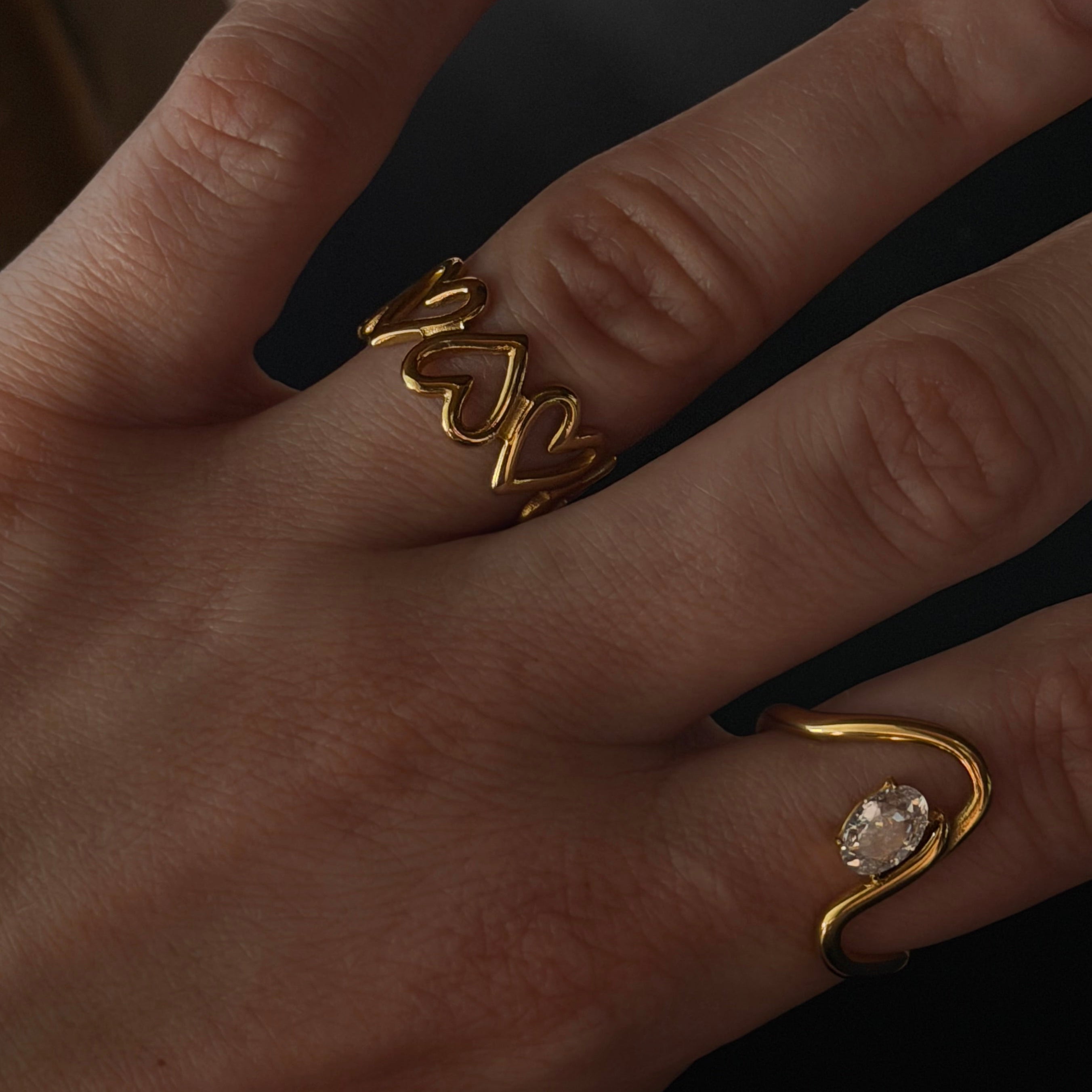 Hand wearing two gold rings with a dark background