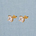 Gold stud earrings with clear gemstones on a light blue textured background
