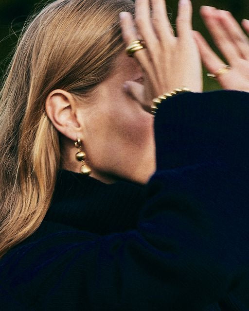 Close-up of a person wearing gold earrings and rings with a blurred background