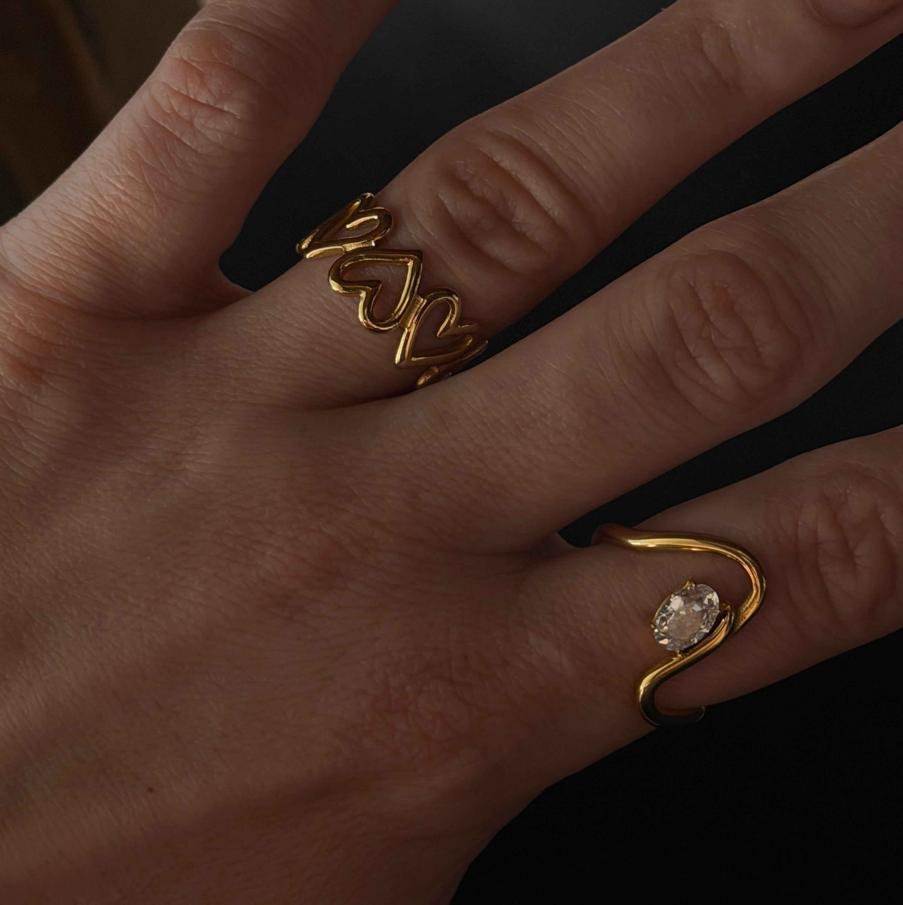 Hand wearing two gold rings with a dark background